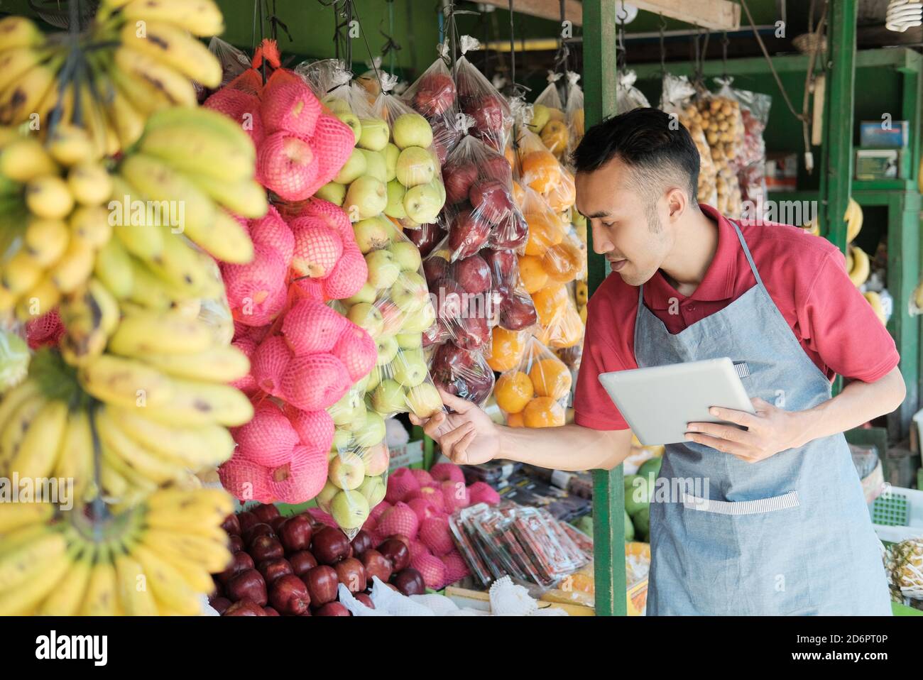 un proprietario di un negozio di sesso maschile che tiene un tablet digitale mentre osserva frutta fresca in un negozio di frutta Foto Stock