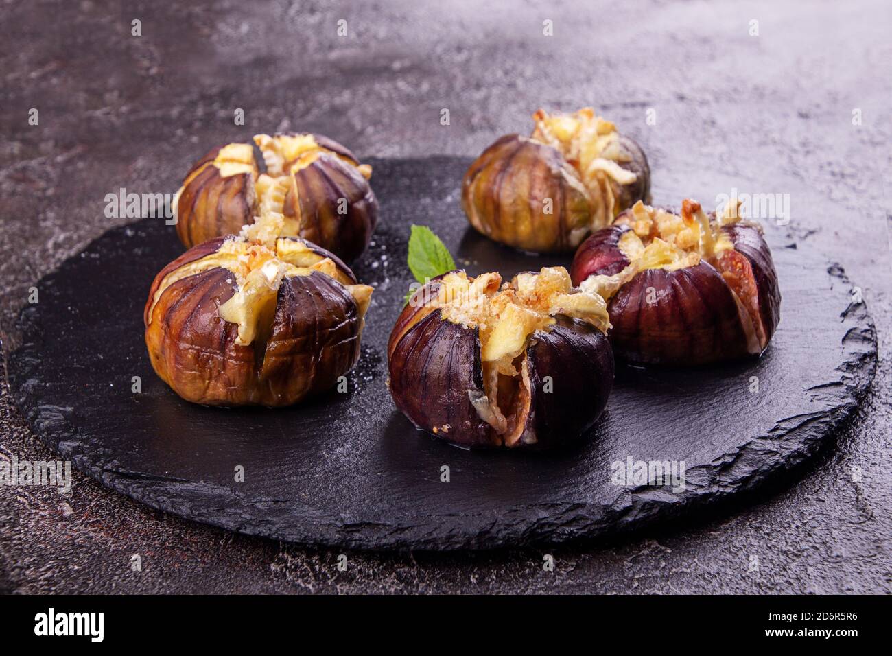 Fichi maturi cotta con latte di vacca Formaggio Brie e camambert e spolverati con briciole di pane decorato con foglie di menta sulla pietra nera dello sfondo. Healt Foto Stock