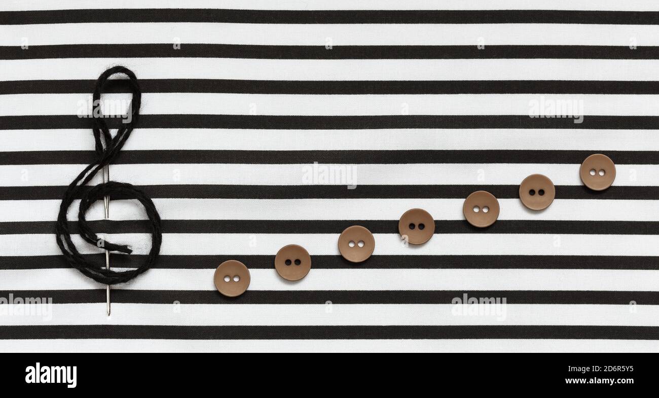 Treble clef, ago e bottoni su tessuto a righe. Foto Stock