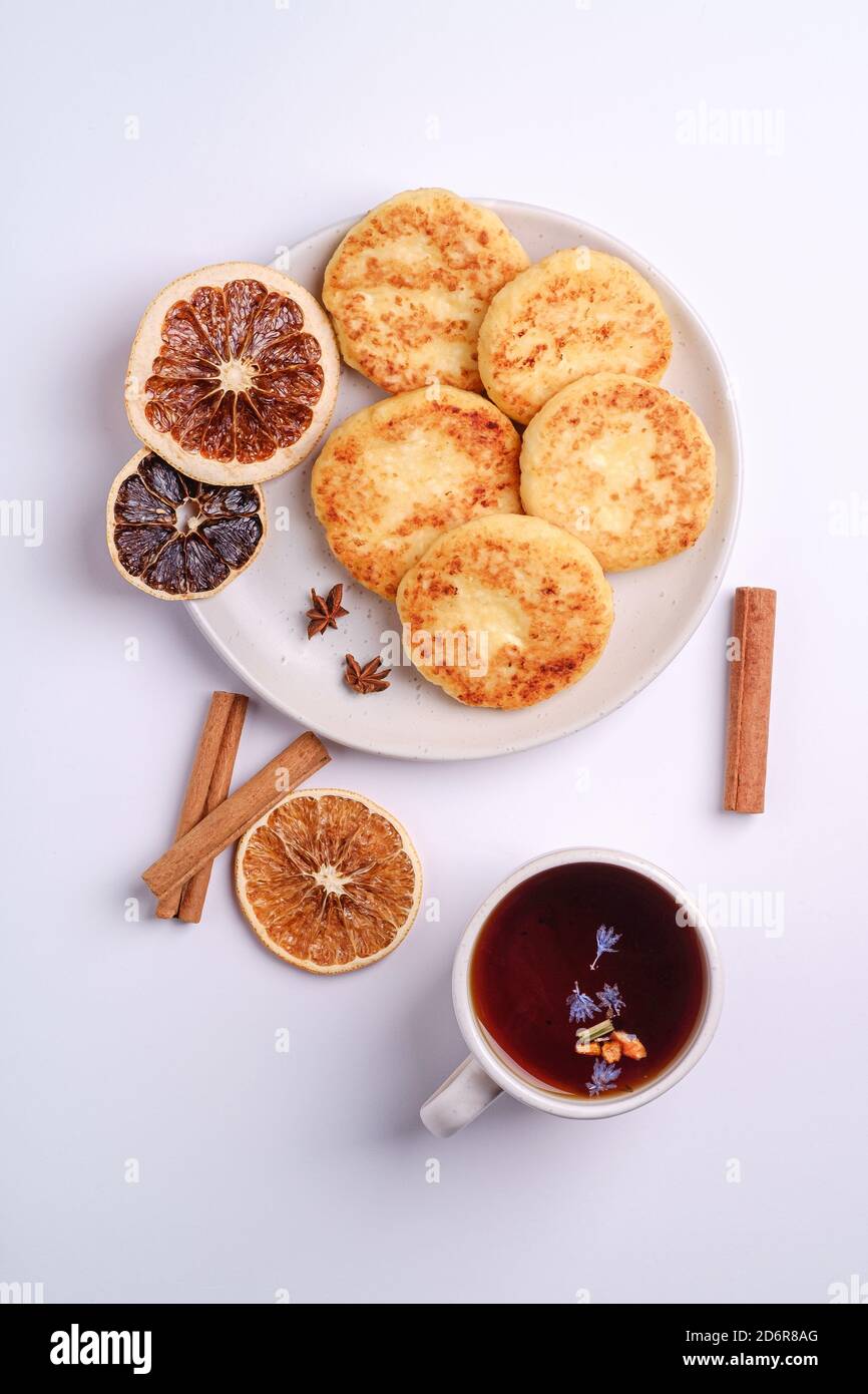 Frittelle di formaggio cottage con tè nero aromatico caldo, umore della colazione di Natale con anice e cannella su sfondo bianco, vista dall'alto Foto Stock