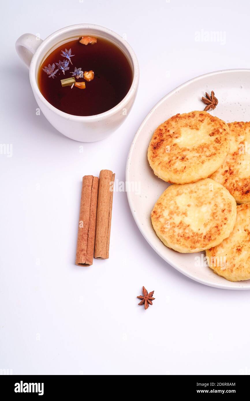 Frittelle di formaggio cottage con tè nero aromatico caldo, umore della colazione di Natale con anice e cannella su sfondo bianco, vista dall'alto Foto Stock