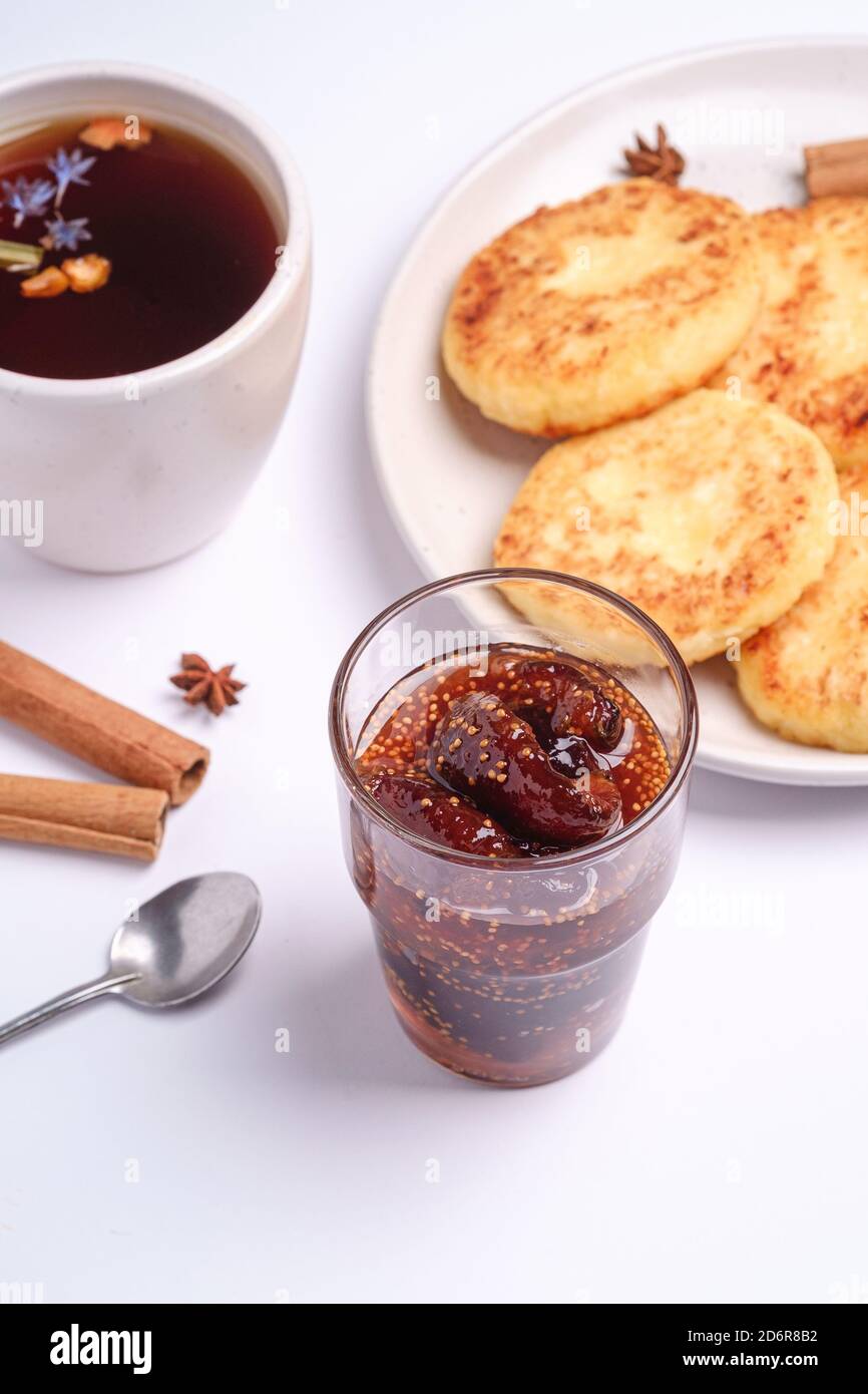 Frittelle di formaggio cottage con marmellata di fichi e tè nero aromatico caldo, umore della colazione di Natale con anice e cannella su sfondo bianco, vista angolare Foto Stock