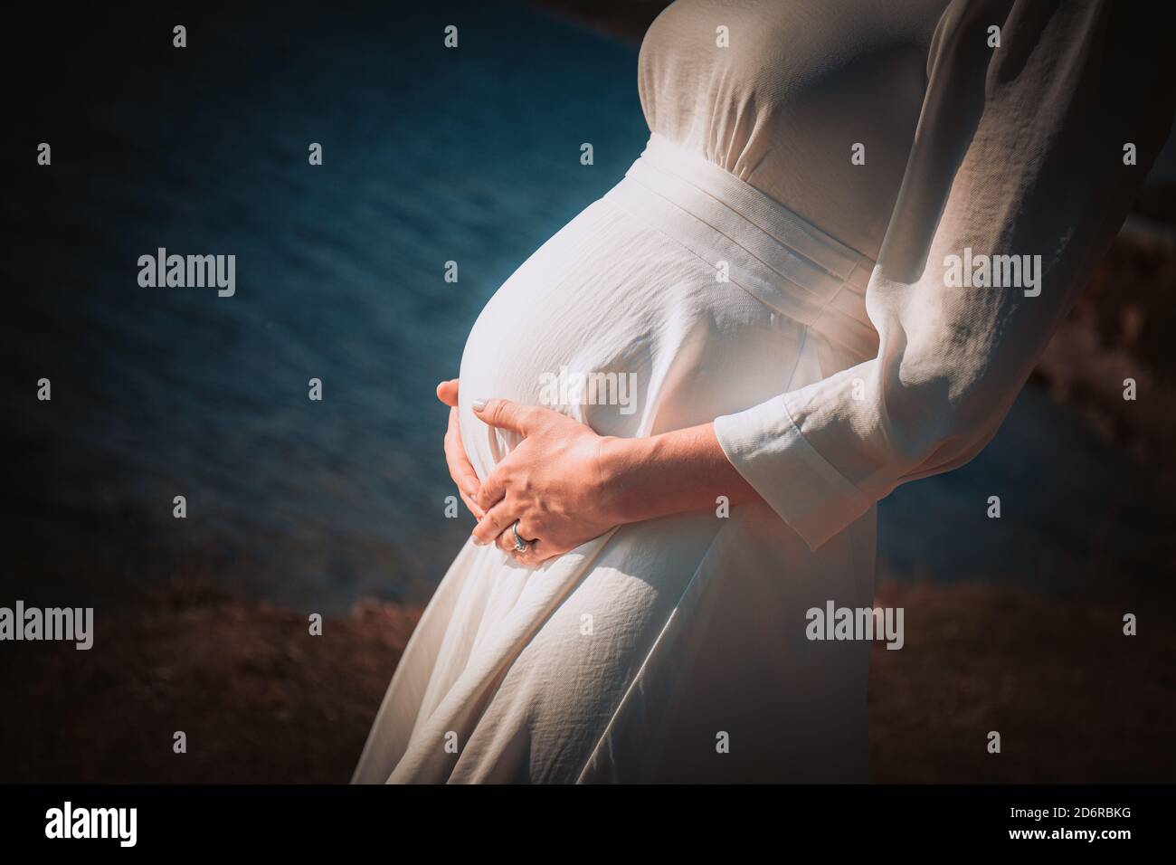 Una donna incinta in un vestito bianco le tiene le mani sul ventre. Il concetto di gravidanza, maternità, preparazione e attesa. Primo piano Foto Stock