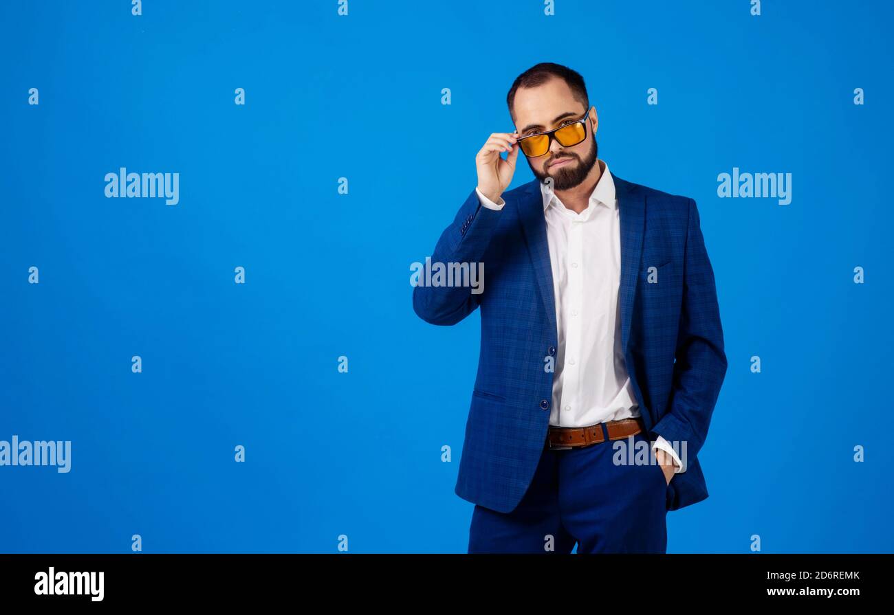 Giovane uomo che indossa occhiali da sole in un classico vestito blu sopra uno sfondo blu Foto Stock