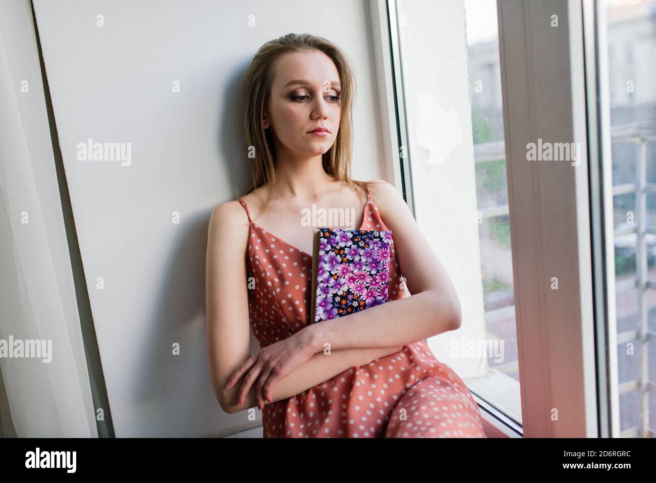 Pensive Dreamy femmina tenere libro a casa guardando grande finestra sognare, pensieroso giovane donna, studente Foto Stock