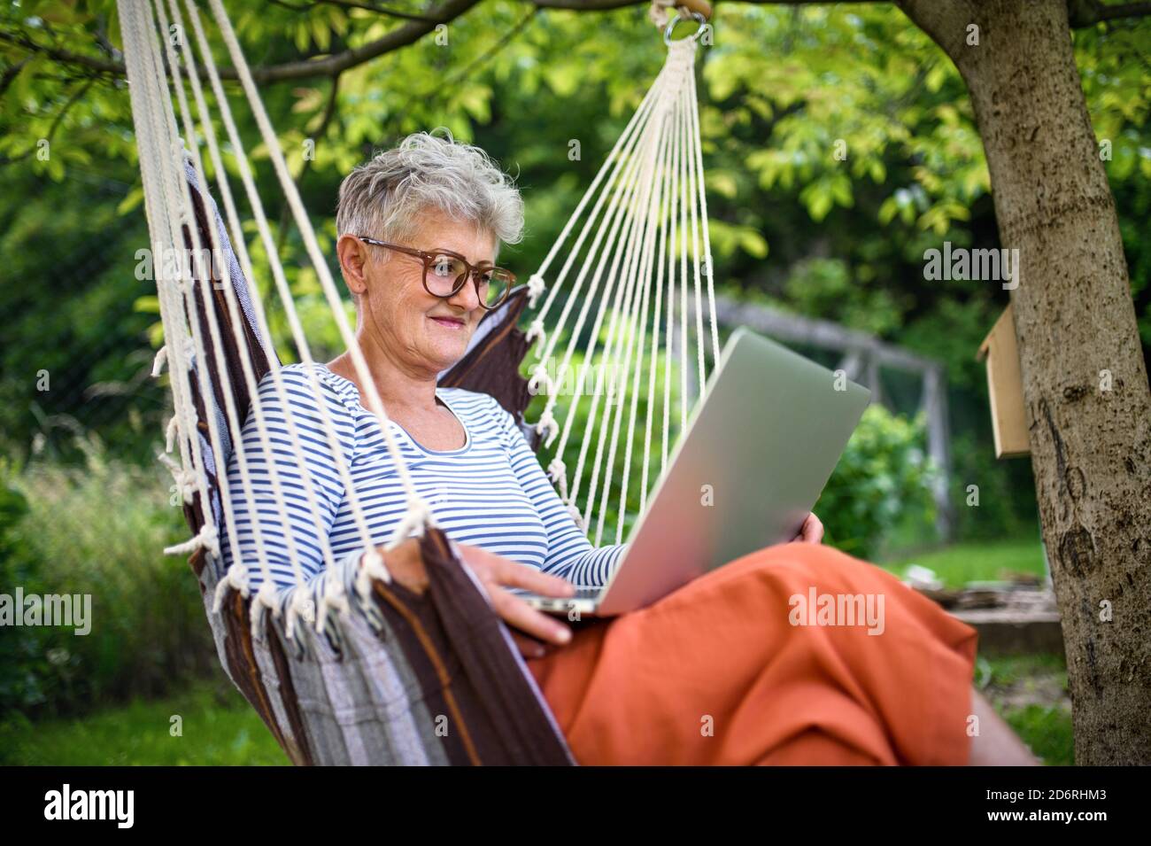 Ritratto di donna anziana attiva con computer portatile che lavora all'aperto in giardino, concetto di home Office. Foto Stock