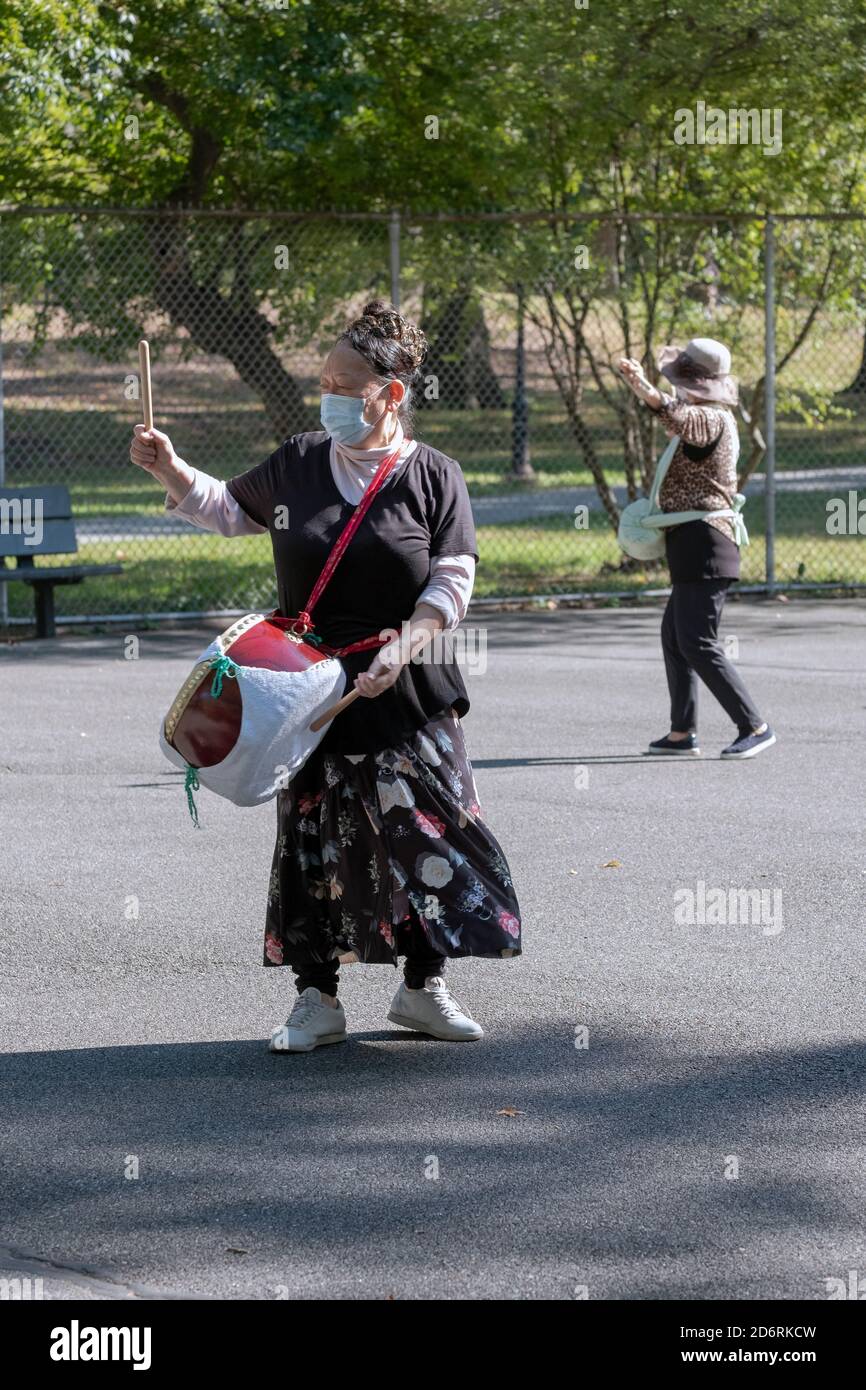 I membri asiatici americani di un ensemble di batteria si provano in un parco a Queens, New York City mentre indossano una maschera chirurgica. Foto Stock
