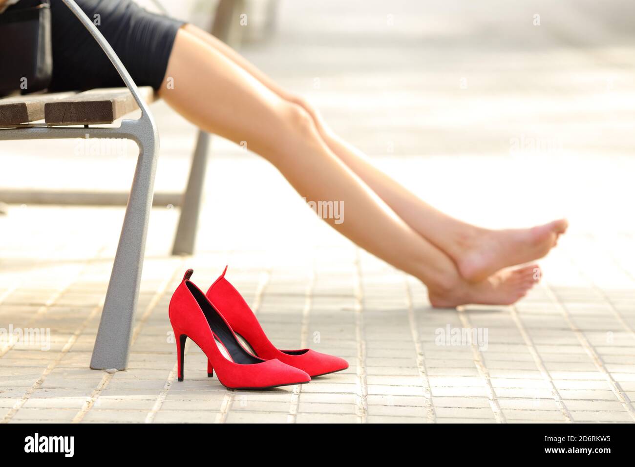 Vista laterale ritratto di una donna gambe decolorante rosso tacchi alti e poggiati su una panchina nella via Foto Stock