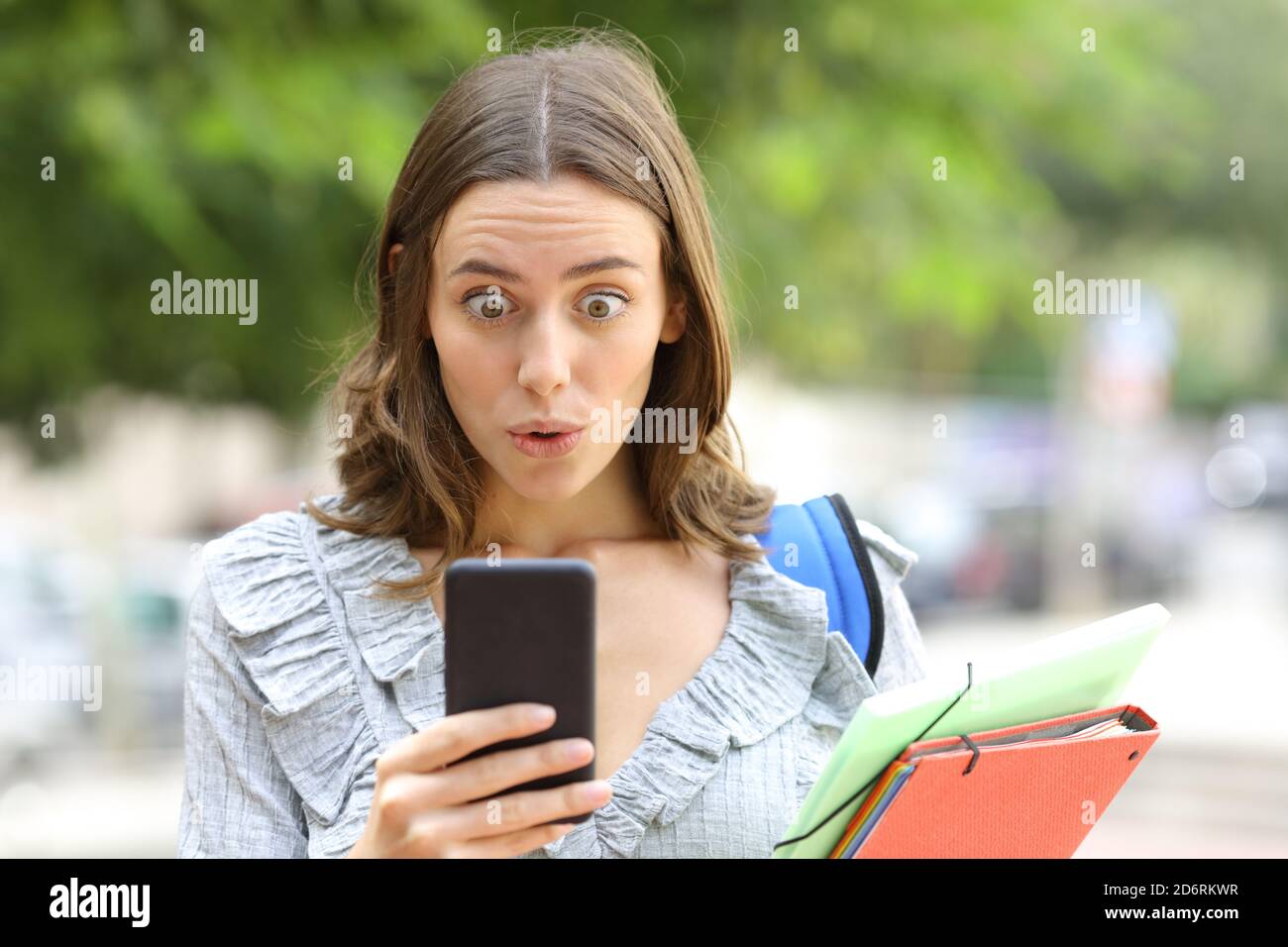Vista frontale ritratto di uno studente sorpreso che controlla il telefono cellulare in strada Foto Stock