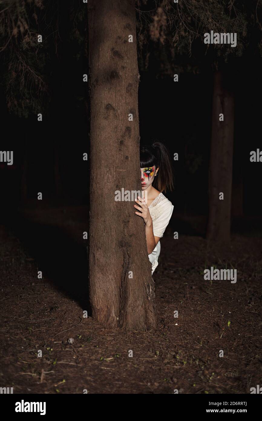 Femmina creepy con faccia verniciata e lenti a contatto striscianti Di notte  su Halloween dietro un albero Foto stock - Alamy