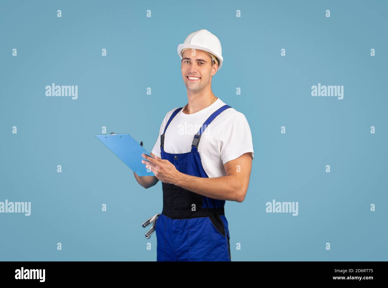 Riparazione e ristrutturazione. Un handyman sorridente in elmetto che si pone su sfondo blu Foto Stock