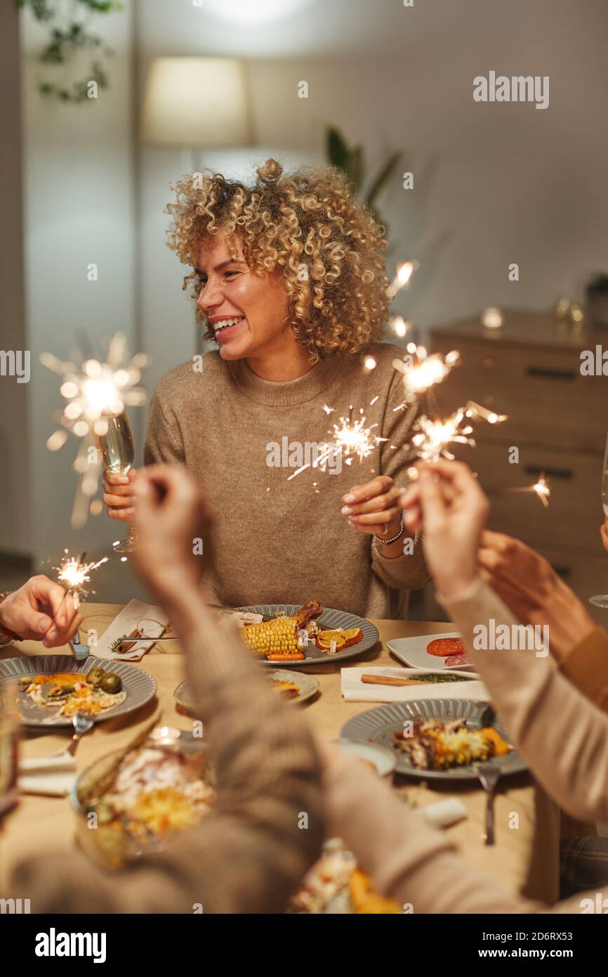 Ritratto verticale di spensierata donna mista che tiene gli sparklers mentre si gode cena e festa con amici e famiglia Foto Stock