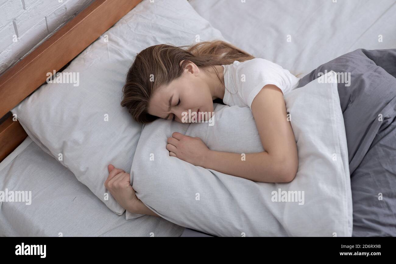 Vista dall'alto della giovane donna depressa sdraiata a letto e. abbracciando il suo cuscino Foto Stock