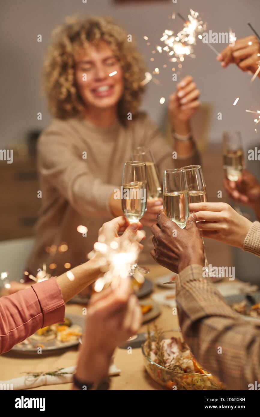 Primo piano verticale di persone che tostano con bicchieri di champagne mentre cena con amici e familiari e con gli sparklers Foto Stock