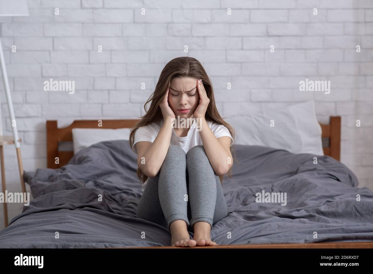 Infelice signora millenaria seduta sul letto e massaggiando i suoi templi, avendo mal di testa o depressione Foto Stock
