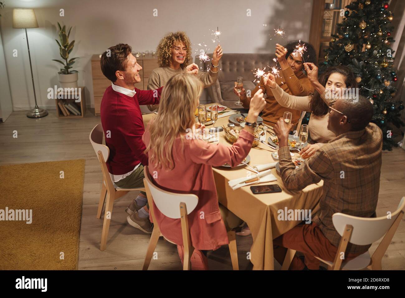 Vista grandangolare delle persone che brindano con bicchieri di champagne mentre si gusta la cena con gli amici e la famiglia, mentre si tengono gli sparklers, copy space Foto Stock
