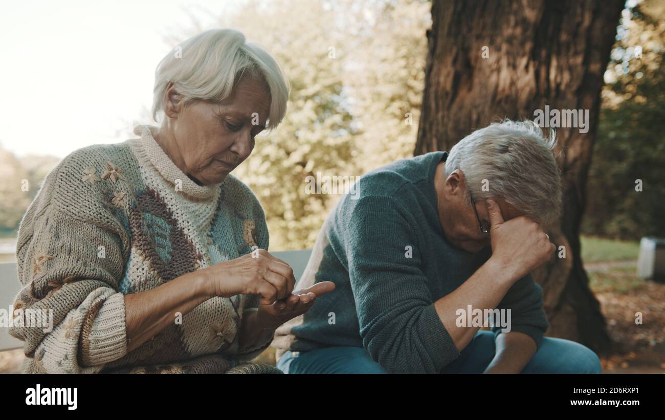 Anziana coppia preoccupata seduta sulla panchina in disperazione. Donna che conta le ultime monete. Foto di alta qualità Foto Stock