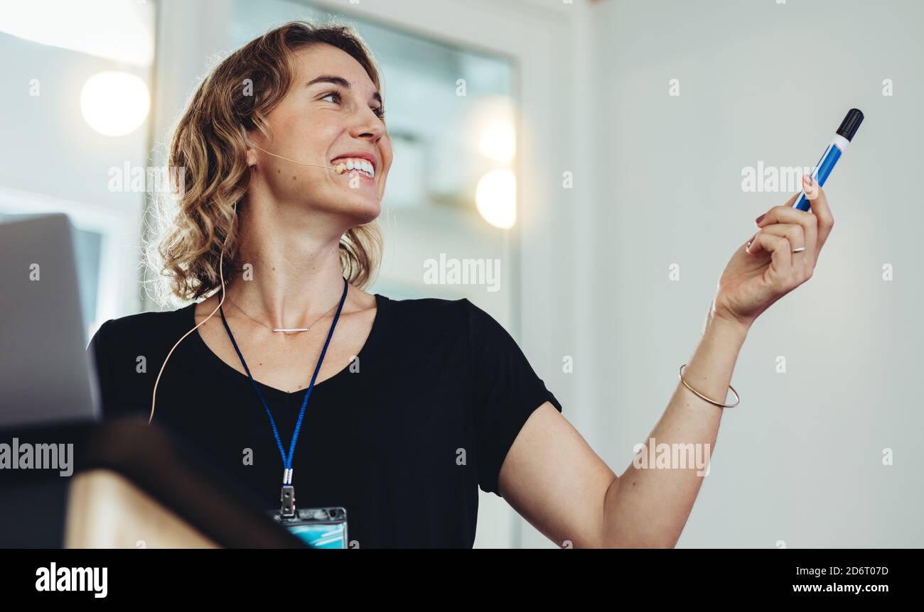 Donna d'affari sorridente che punta allo schermo del proiettore durante la sua presentazione. Donna imprenditore che dà la presentazione ad un seminario. Foto Stock
