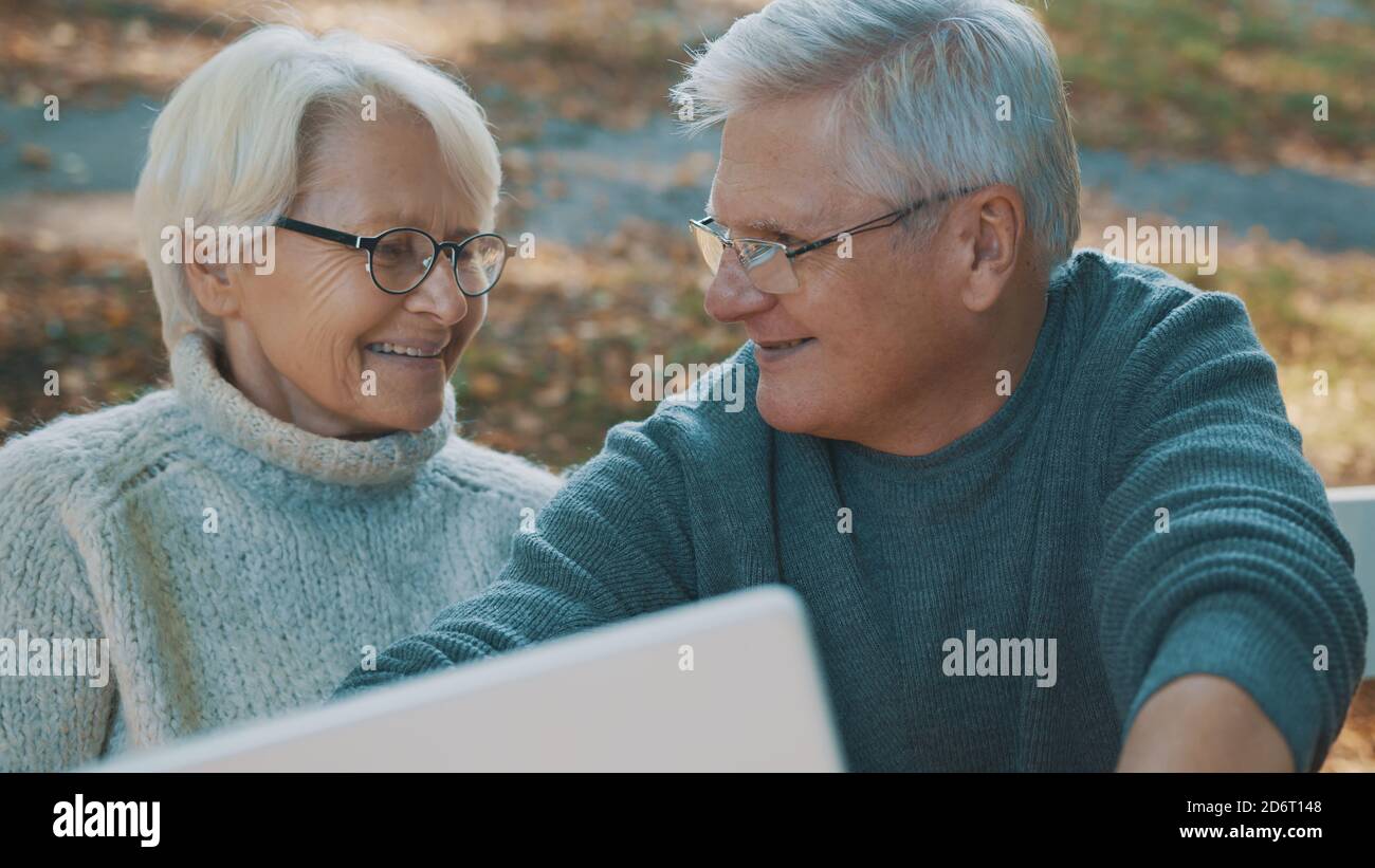 Coppia matura in amore prendendo selfie in foresta il giorno d'autunno. Videochiama o sfoglia le vecchie foto. Foto di alta qualità Foto Stock