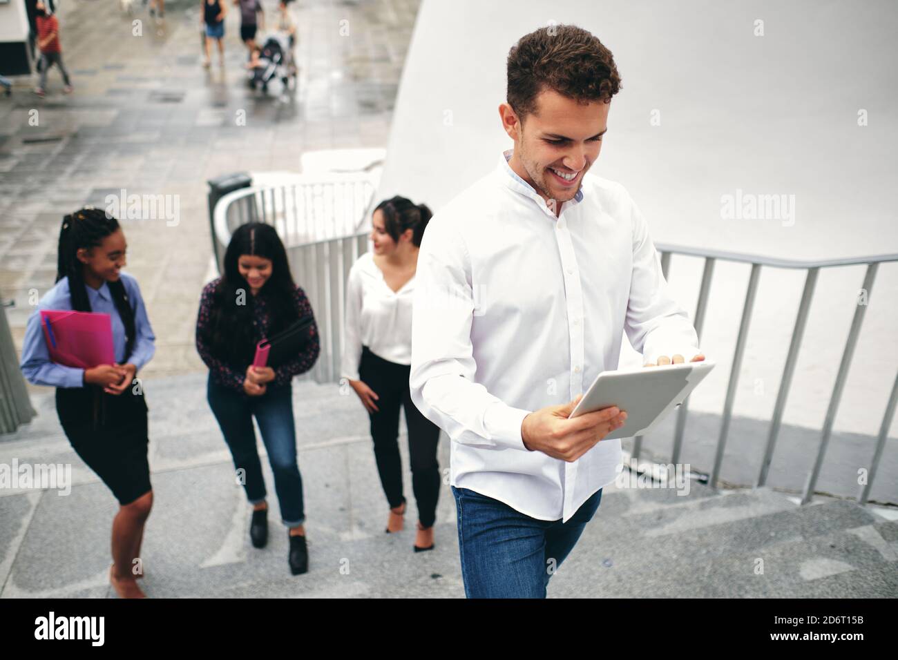 Da sotto di uomo allegro che naviga in Internet sul tablet mentre in piedi sulle scale dietro gli amici sulla strada Foto Stock