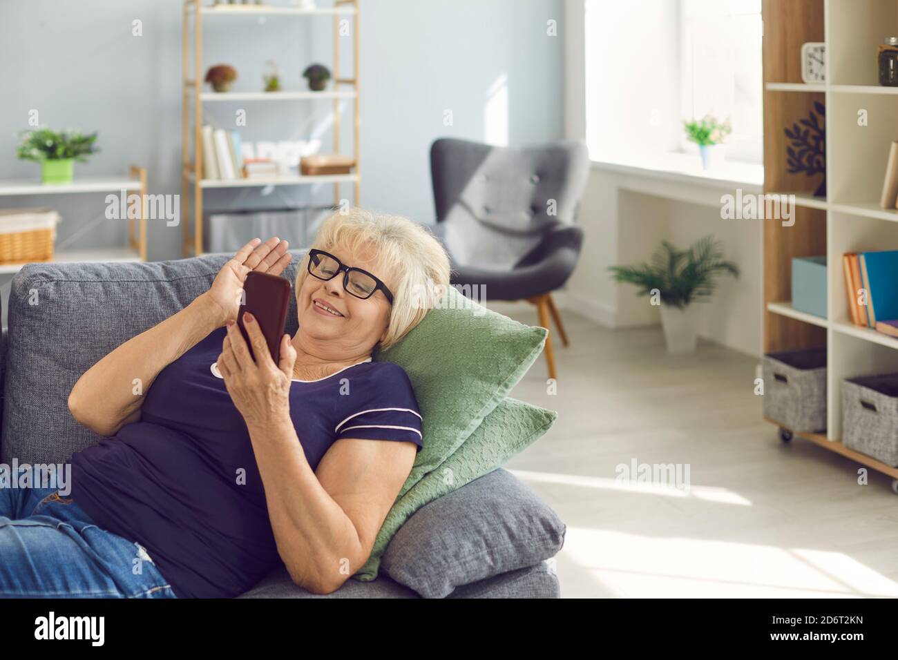 Felice donna anziana sorridente sdraiata sul divano e che parla videochiama con il telefono con la famiglia Foto Stock