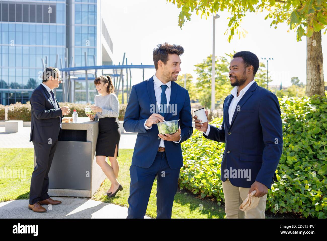 Positivi giovani colleghi diversi in abiti formali sorridendo mentre hanno pausa pranzo insieme sulla strada il giorno di sole Foto Stock