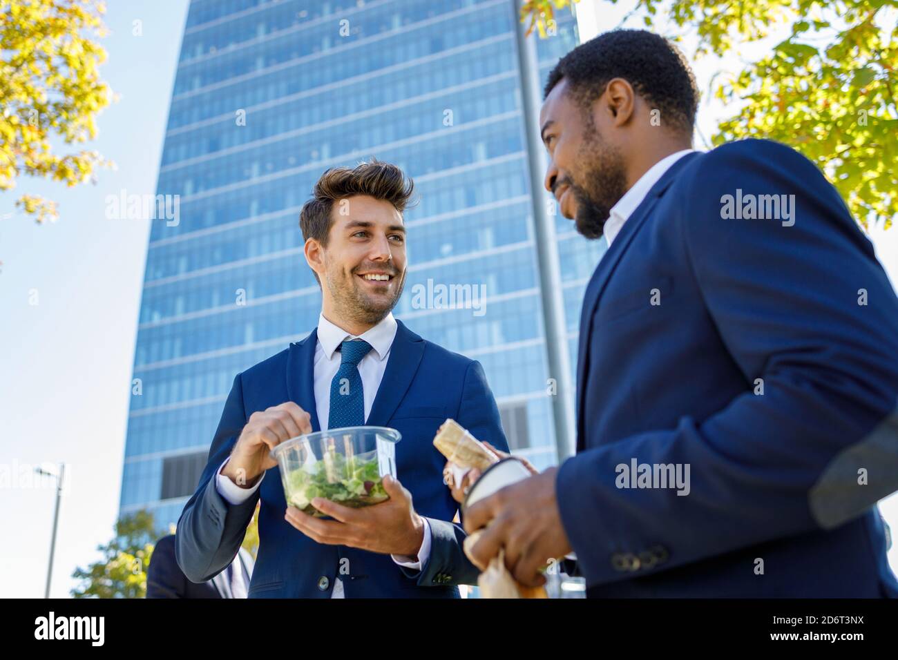 Positivi giovani colleghi diversi in abiti formali sorridendo mentre hanno pausa pranzo insieme sulla strada il giorno di sole Foto Stock