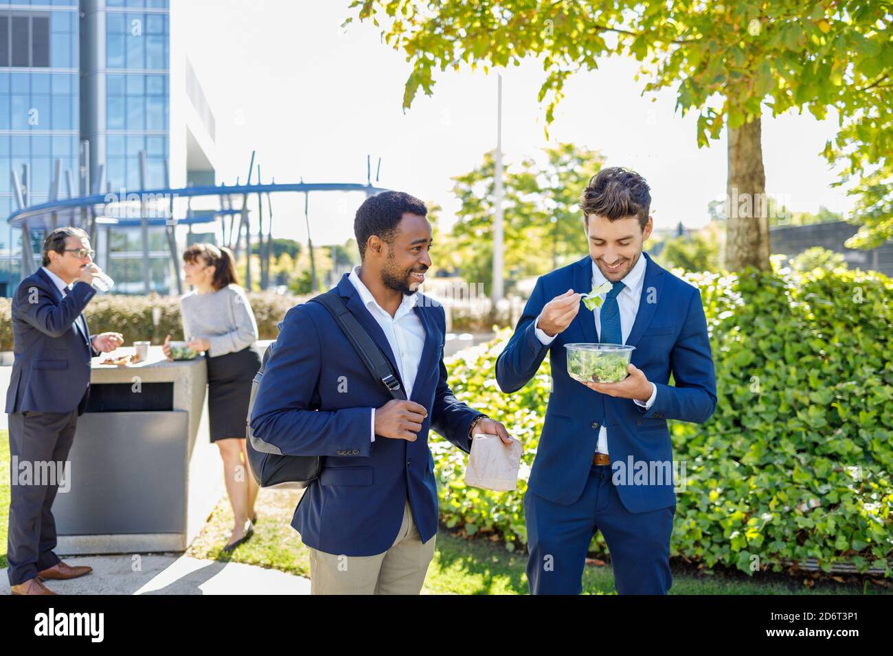 Positivi giovani colleghi diversi in abiti formali sorridendo mentre hanno pausa pranzo insieme sulla strada il giorno di sole Foto Stock