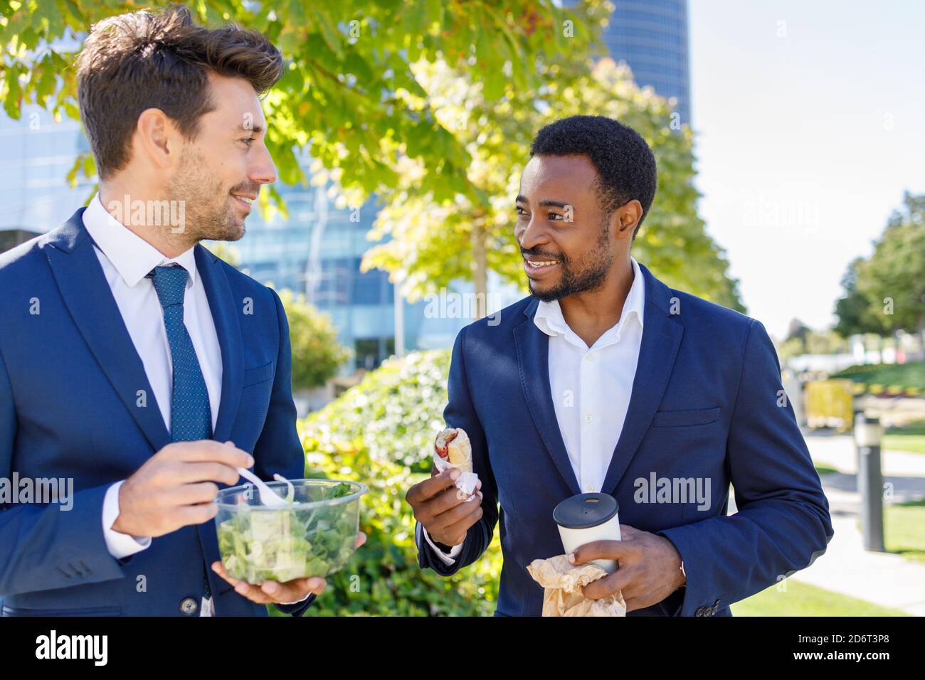 Positivi giovani colleghi diversi in abiti formali sorridendo mentre hanno pausa pranzo insieme sulla strada il giorno di sole Foto Stock