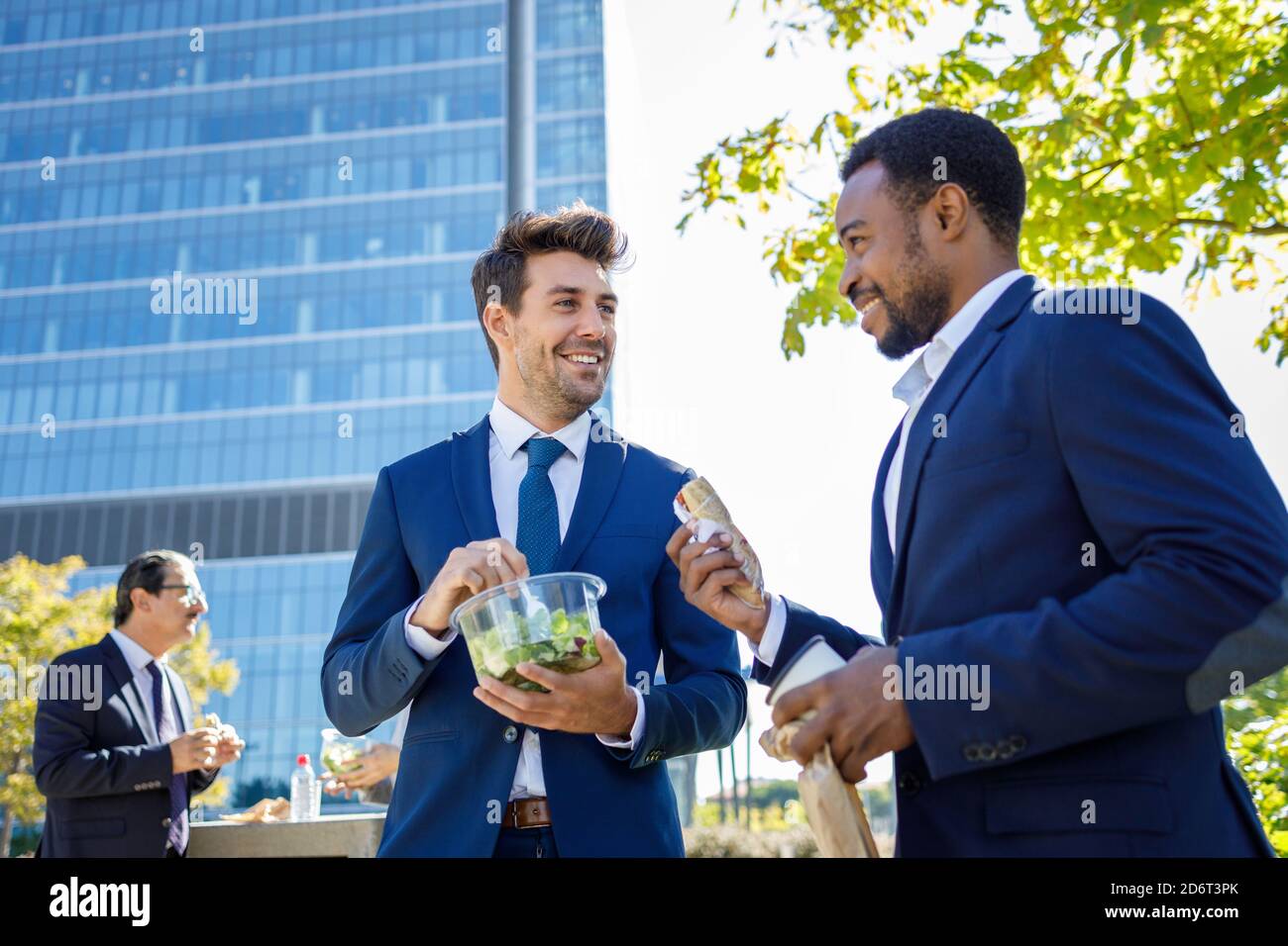 Positivi giovani colleghi diversi in abiti formali sorridendo mentre hanno pausa pranzo insieme sulla strada il giorno di sole Foto Stock