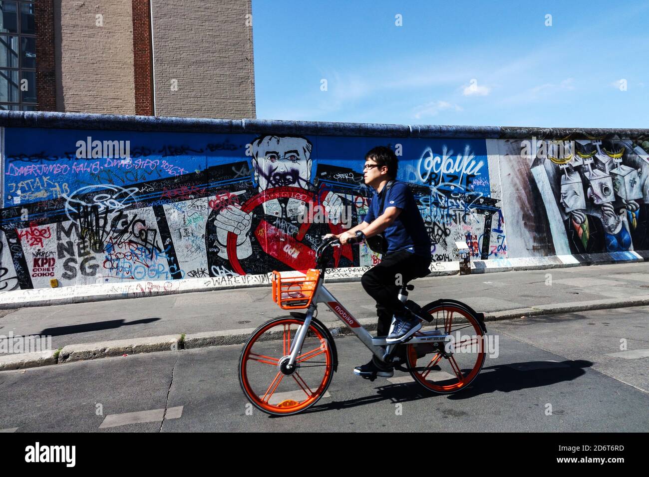 Uomo giro in bicicletta Berlino muro graffiti East Side Gallery Berlino Germania Friedrichshain Street art Berlino bike wall Foto Stock