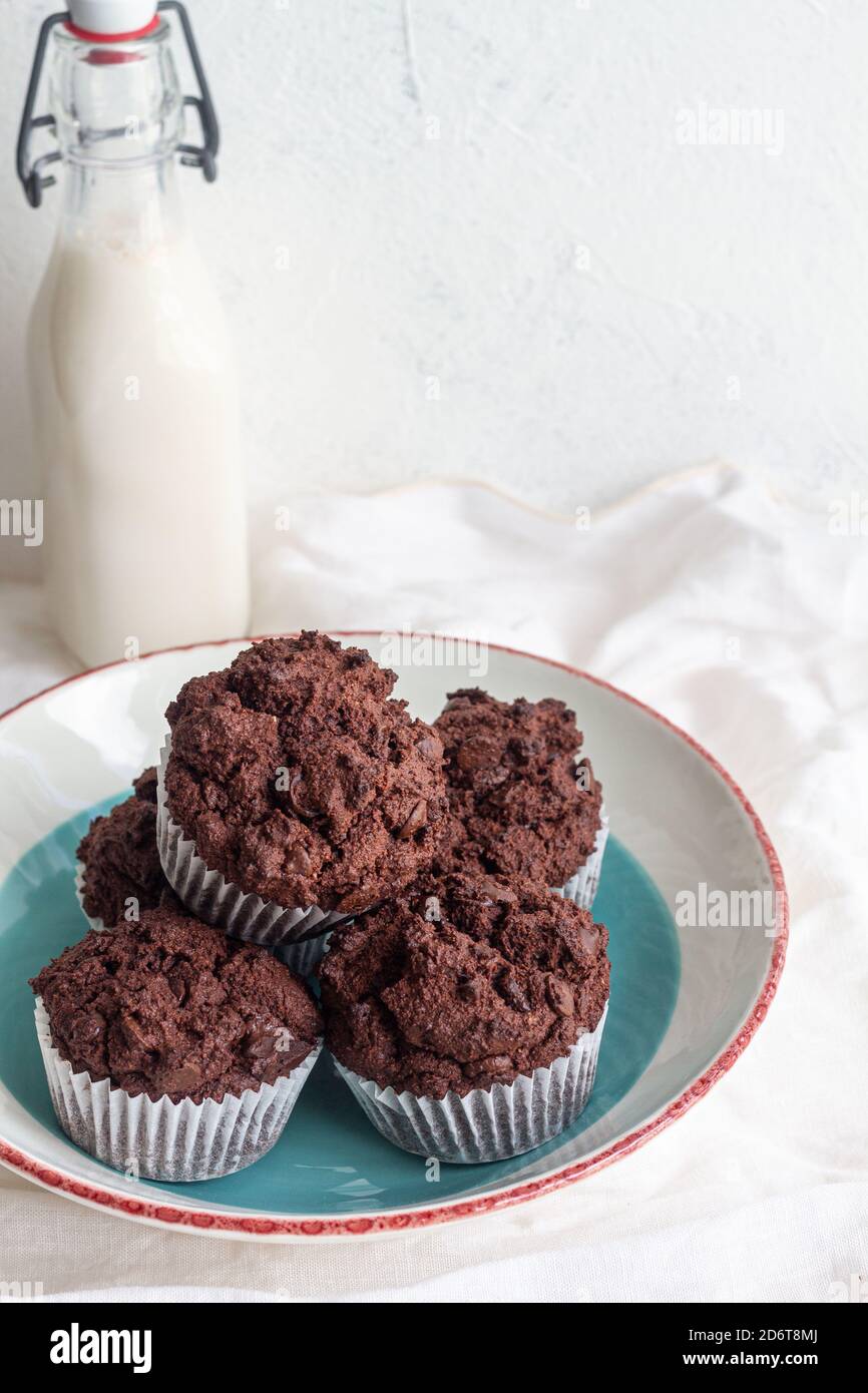 Gustosi cupcake di cioccolato dolce ad angolo alto colti sul piatto vicino vasetto con latte fresco in cucina leggera Foto Stock