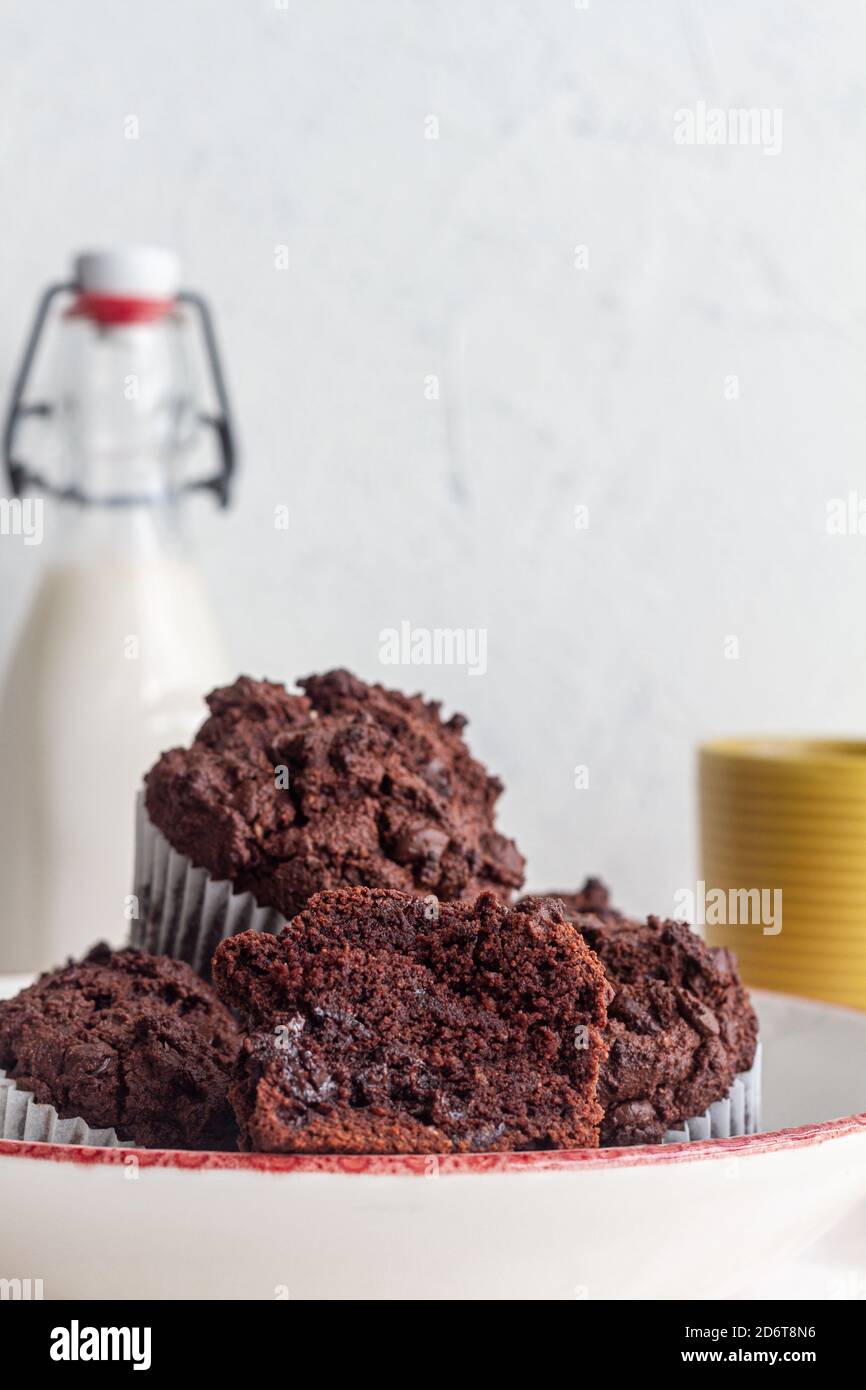 Gustosi cupcake di cioccolato dolce ad angolo alto colti sul piatto vicino vasetto con latte fresco in cucina leggera Foto Stock