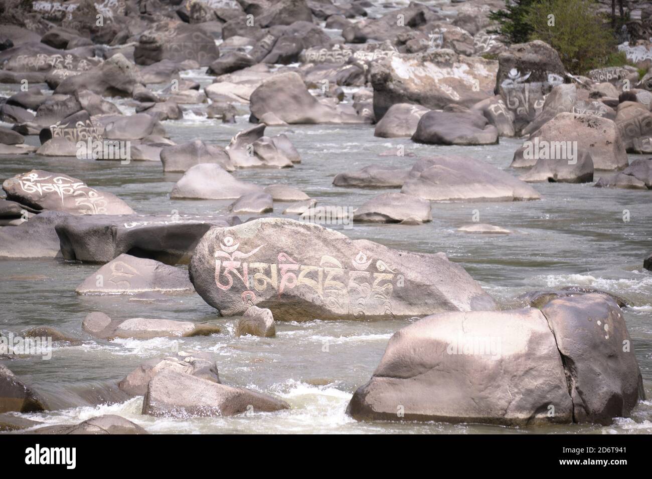 Sanscrito mantra Om mani Padme Hum inciso sulla superficie di grandi pietre grigie nel fiume di montagna nel villaggio di Baiyu in Cina Foto Stock