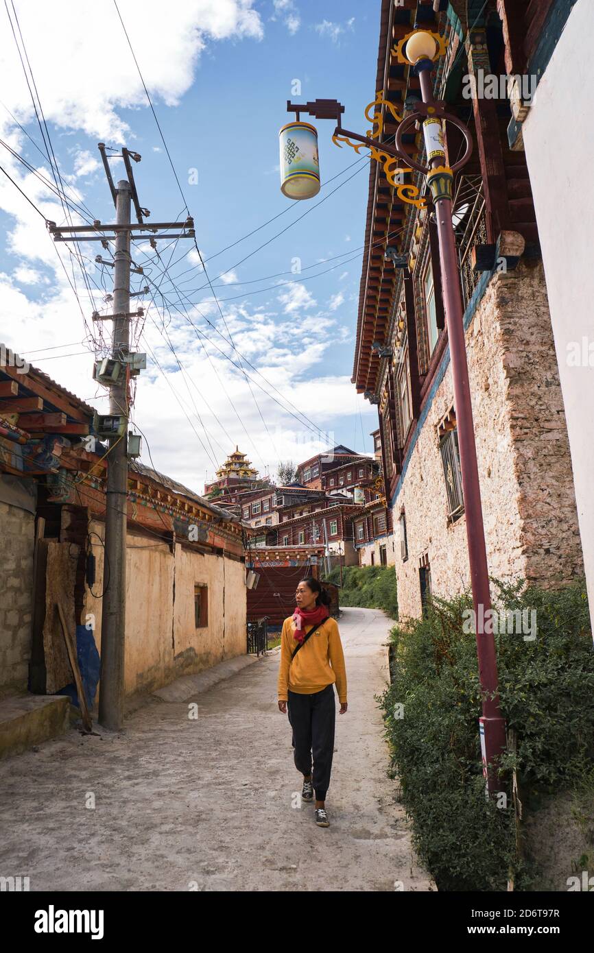 Corpo pieno di turista femminile in abbigliamento casual che guarda via mentre camminando su strada lastricata tra piccole case sotto sudicio fili e cielo azzurro Foto Stock