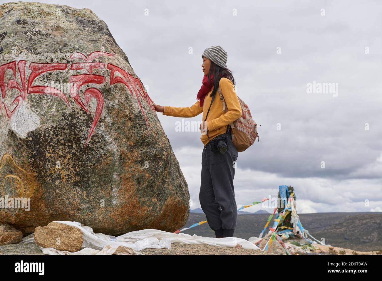 Vista laterale del corpo completo del turista femminile in abiti caldi e cappello guardando grande pietra con Om mani Padme Hum mantra sulla superficie nel villaggio di Baiyu in Foto Stock