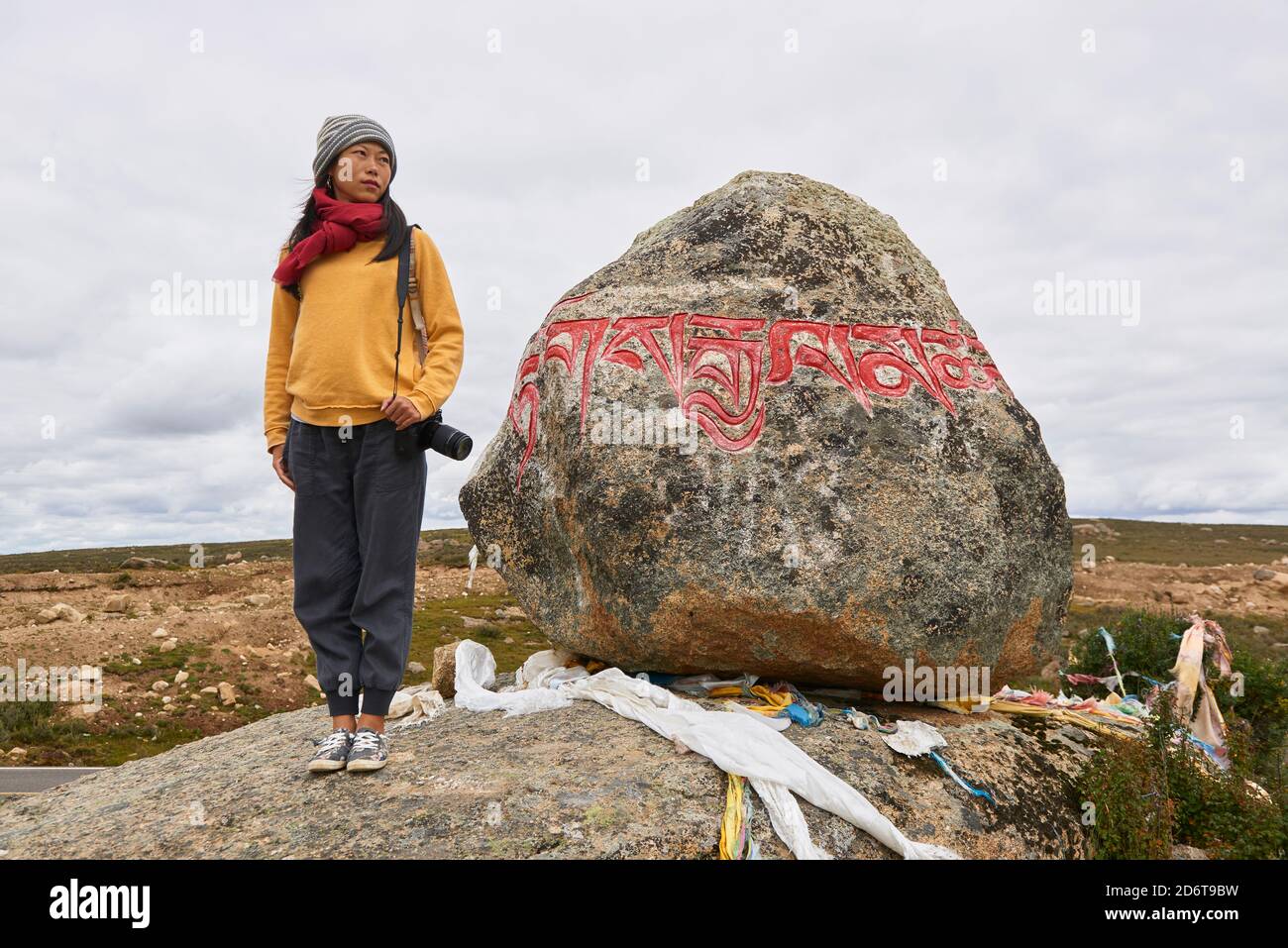 Corpo pieno di turista femminile in abiti caldi e cappello guardando grande pietra con Om mani Padme Hum mantra sulla superficie nel villaggio di Baiyu in Cina Foto Stock