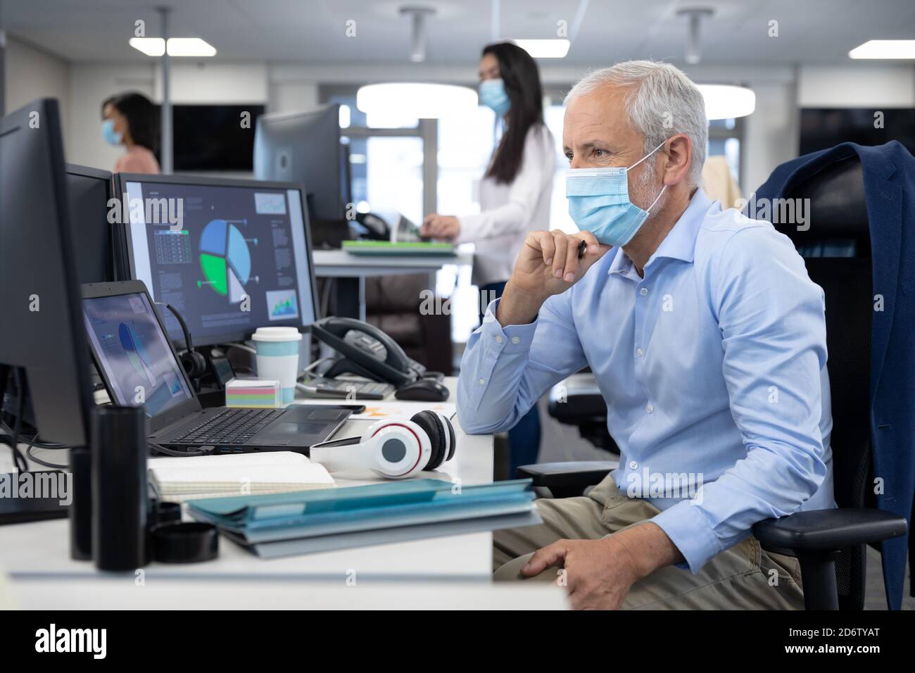 Uomo d'affari senior pensieroso che indossa la maschera seduta sulla sua scrivania in un ufficio moderno Foto Stock