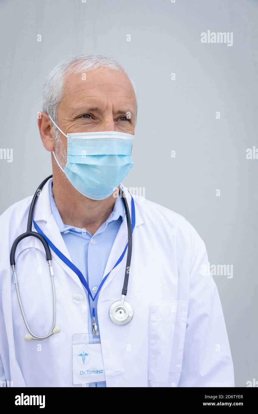 Medico maschile senior che indossa la maschera facciale su sfondo grigio Foto Stock
