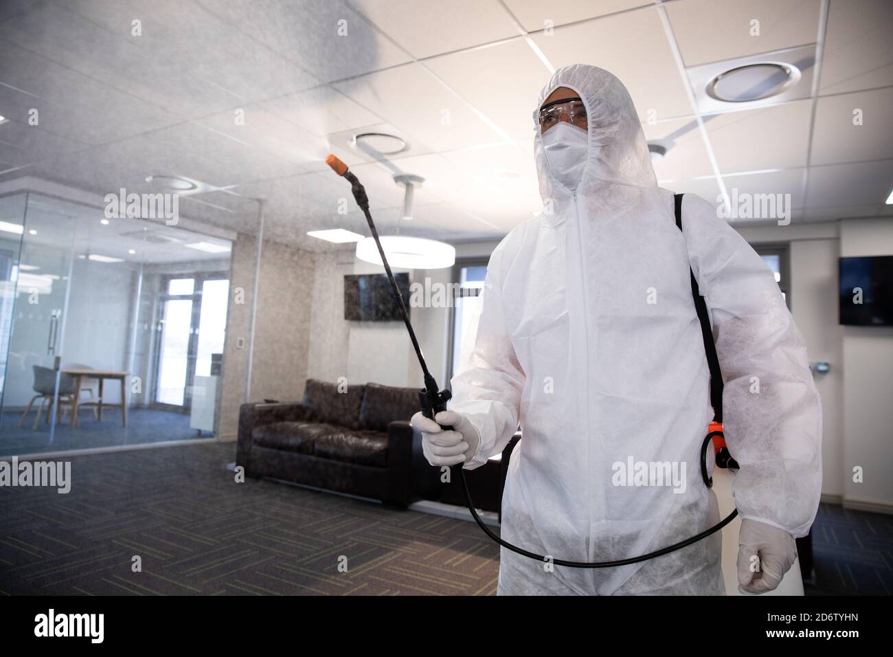 Operatore che indossa tuta protettiva, maschera per il viso e guanti igienizzanti per ufficio utilizzando uno spray disinfettante antibatterico. Igiene sul posto di lavoro durante Coronav Foto Stock