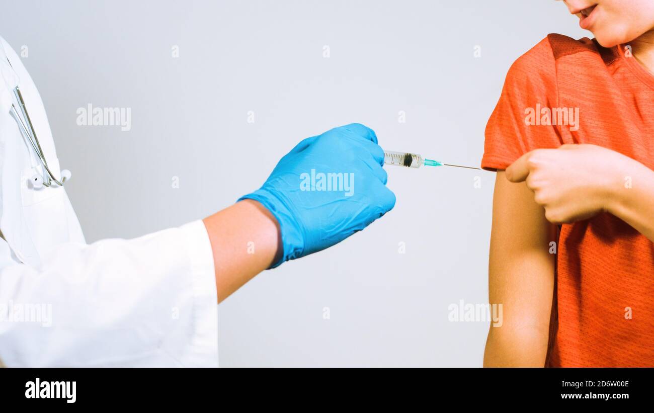 Medico che vaccina rifiutando il bambino per Coronavirus in clinica. Siringa in un guanto di protezione mani. Foto Stock