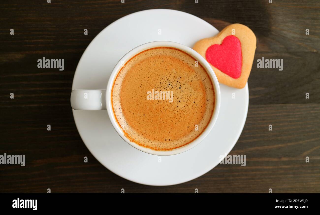 Vista dall'alto di una tazza di caffè caldo con cuore Cookie sagomato su tavolo di legno marrone scuro per il concetto Di AMORE Foto Stock