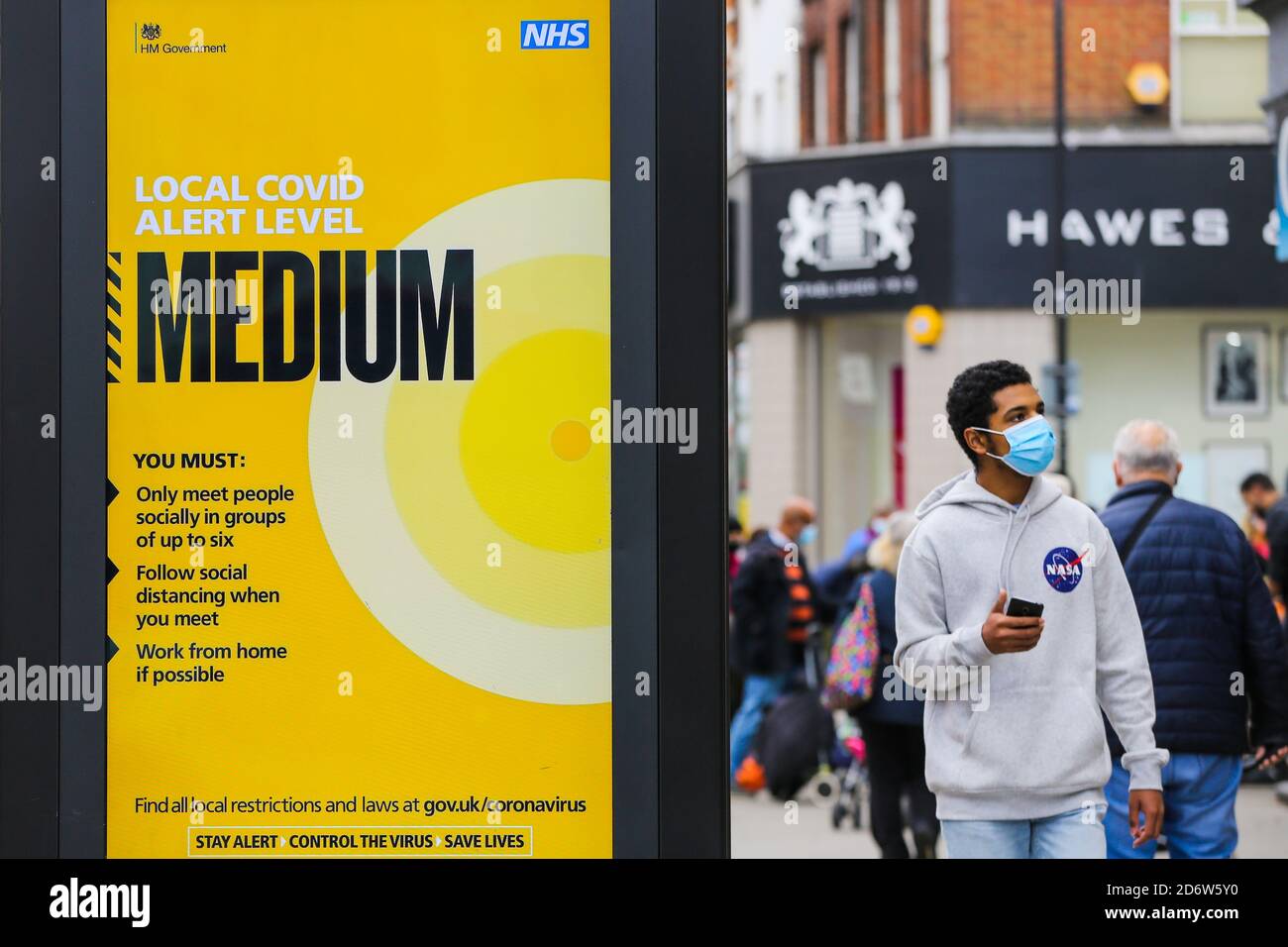 Un uomo che indossa una maschera facciale oltrepassa un poster di informazioni pubbliche sul livello locale di COVID-19, che è medio a Londra, mentre la capitale passa a COVID-19 di secondo livello restrizioni a seguito dell'annuncio da parte dei governi di misure più severe per gestire i casi in aumento. Foto Stock