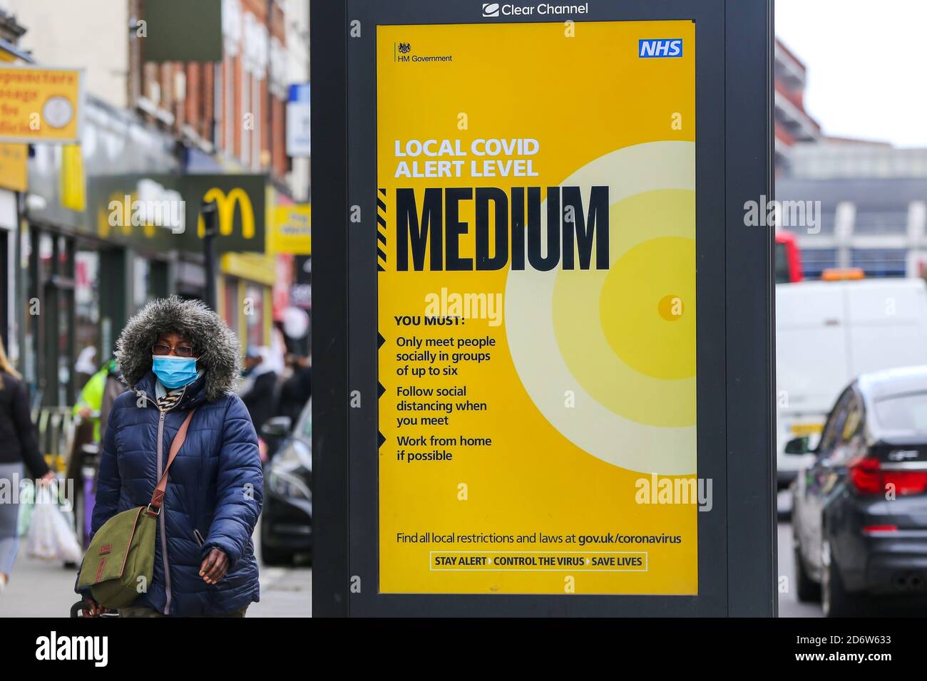 Una donna che indossa una maschera facciale oltrepassa un poster di informazioni pubbliche sul livello locale di COVID-19, che è medio a Londra, mentre la capitale passa a COVID-19 di secondo livello restrizioni a seguito dell'annuncio da parte dei governi di misure più severe per gestire i casi in aumento. Foto Stock