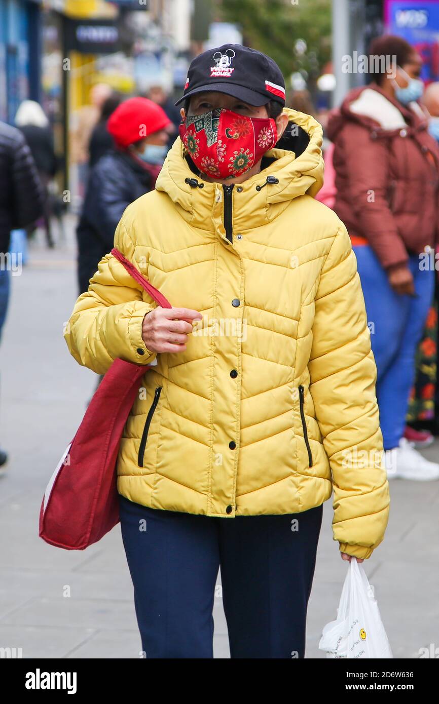 Una donna che indossa una maschera facciale come misura preventiva cammina per strada a Londra mentre la capitale passa alle restrizioni di secondo livello della COVID-19 a seguito dell’annuncio da parte del governo di misure più severe per gestire i casi in aumento. Foto Stock