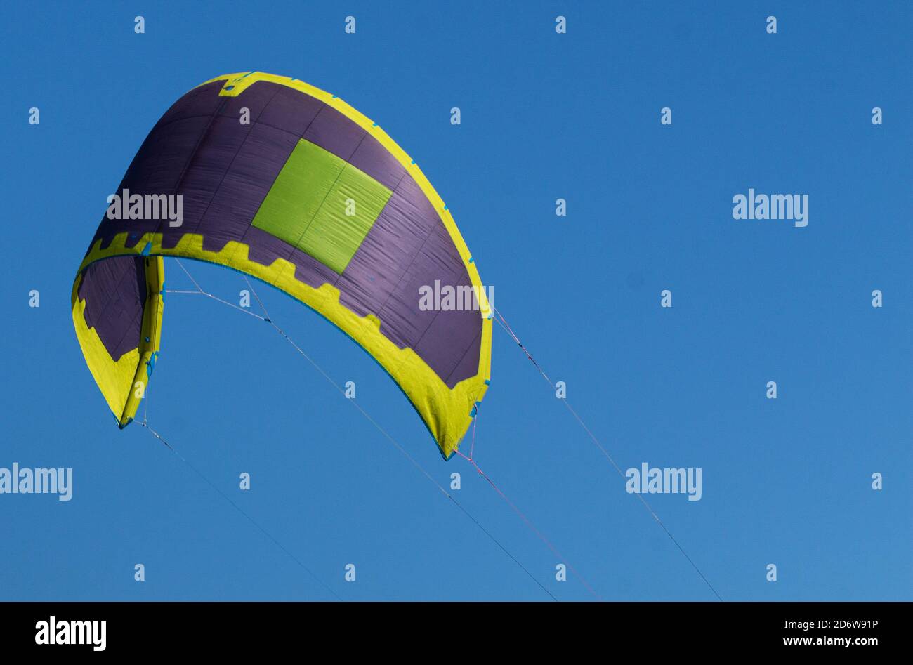 Una vela viola, gialla e verde di un surfista kite nell'aria con un cielo blu profondo come sfondo. Foto Stock