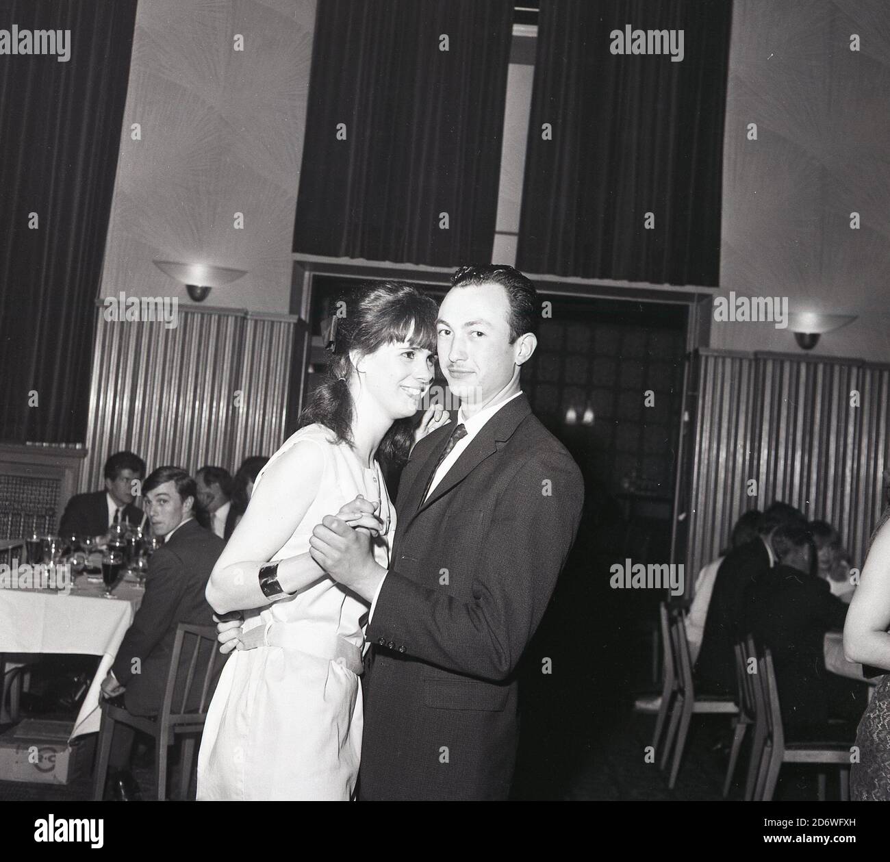 Anni '60, storico, una coppia che si gode una stretta danza in una festa in una grande sala funzioni, Londra, Inghilterra, Regno Unito. Foto Stock