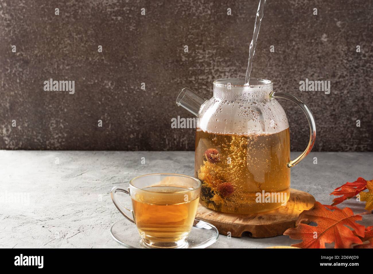 Un vapore d'acqua bollita che si versa in una teiera di vetro con tè in fiore. Cerimonia del tè d'autunno. Foto Stock