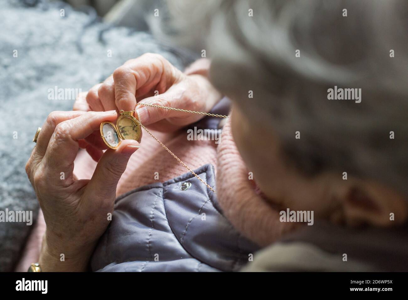 Donna anziana che guarda le foto in un medaglione pendente. Foto Stock