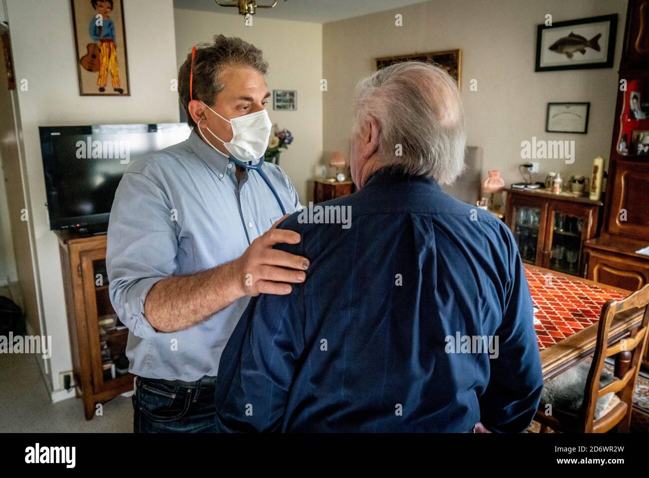 Medico generico che indossa una maschera chirurgica, con paziente a casa, Francia, giugno 2020. Foto Stock